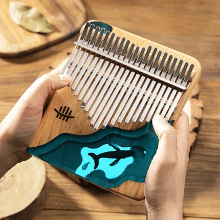 A person playing a 21-key Hluru flat-board kalimba made of maple wood, featuring a beautiful blue resin design of a whale in the ocean.