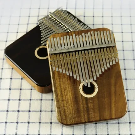 Two LOOP kalimbas, a 17/21 key model in bright Acacia wood and another in dark Rosewood, shown together on a checkered cloth. Caption: Choose your voice: the bright, clear tone of Acacia (front) or the deep, warm resonance of Rosewood (back).