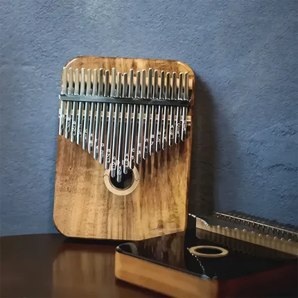 A lifestyle shot of the Acacia wood 21 key kalimba on a table, with a Rosewood model in the background.
