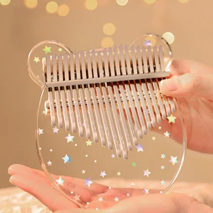 A person holding a transparent bear-shaped 21-key acrylic kalimba with shimmering star decorations.