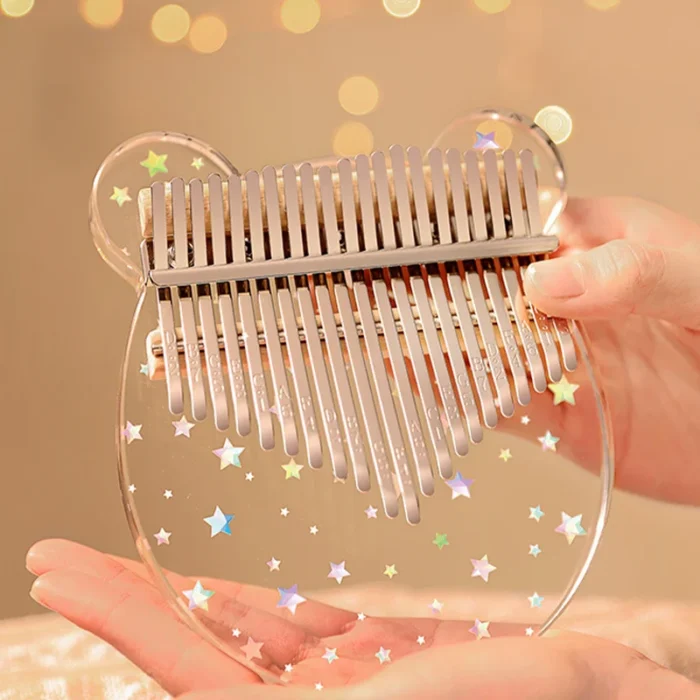A person holding a transparent bear-shaped 21-key acrylic kalimba with shimmering star decorations.