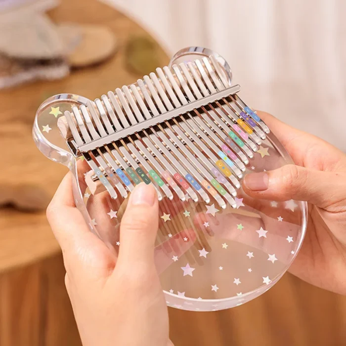 A transparent bear-shaped 17-key acrylic kalimba featuring colorful note stickers from HUASHU.