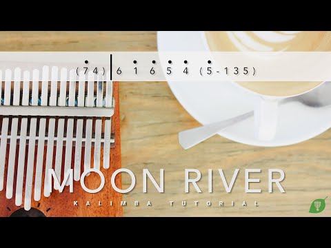 A kalimba and a coffee cup sit on a wooden table with kalimba notes, featuring the moon-river-kalimba-tabs-cover text overlay.